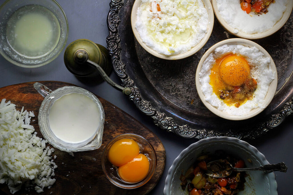 Form a well in ¾ of the egg whites, then layer shallots, tomatoes, yolks, pepper, cheese, butter, and cream.