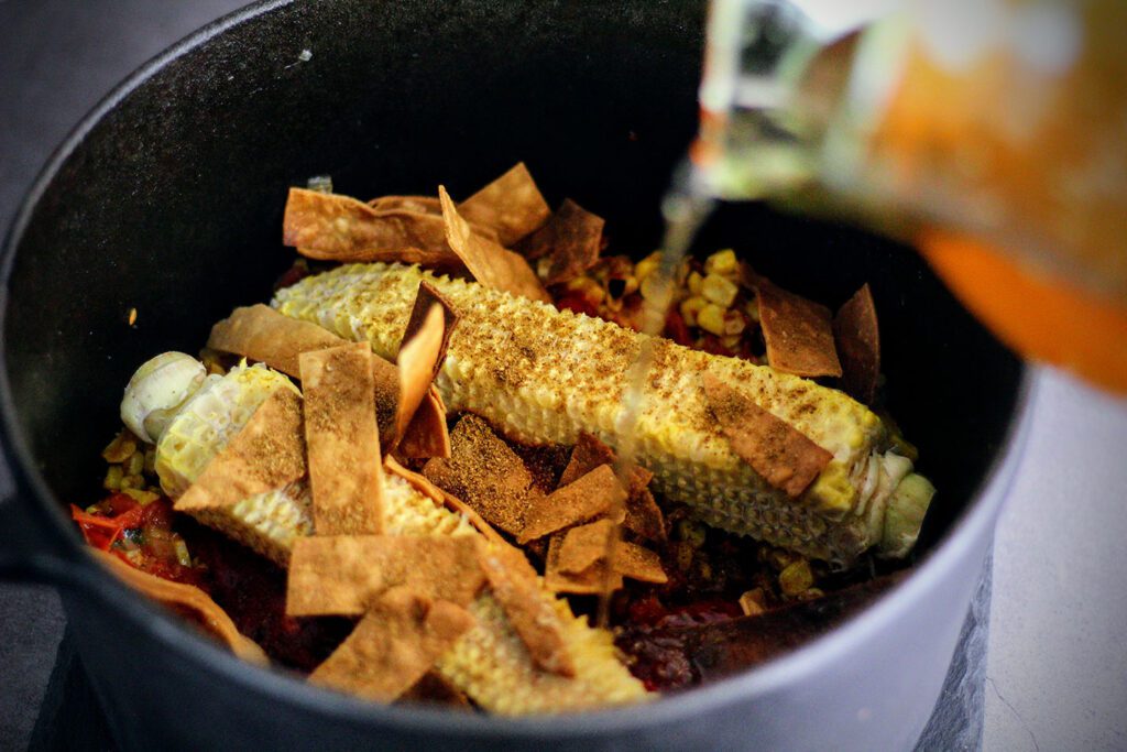 Add vegetables, tortilla strips, Guajillo chile puree, chicken stock, and corn cobs to a pot and reduce by a third. Remove the cobs and blend until smooth.