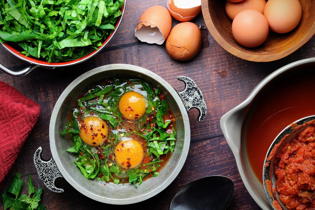 Cover tomatoes with spinach, create indentations, then crack eggs into them before baking.