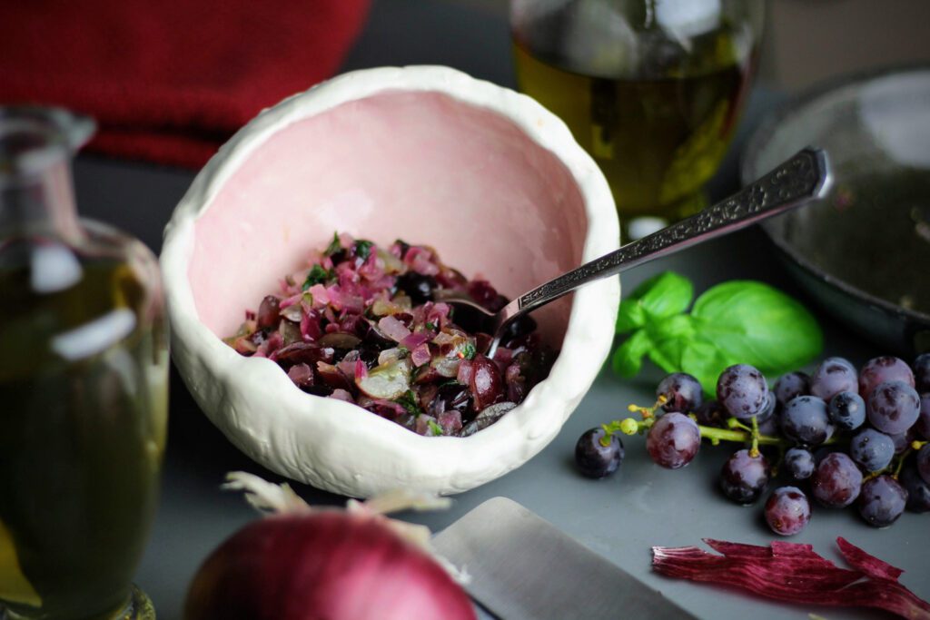 Mix the cooked red onions with grapes, oil, vinegar, and basil to make the relish.