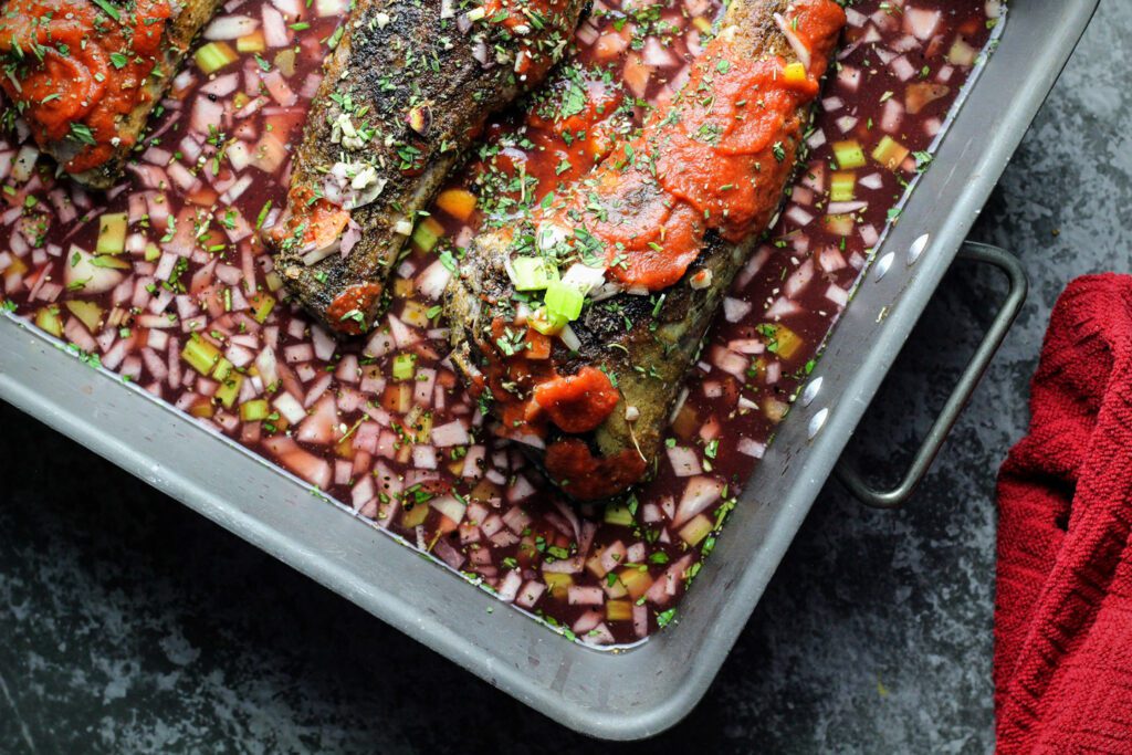 Lamb shanks in a roasting pan with vegetables, red wine, tomato puree, and herbs
