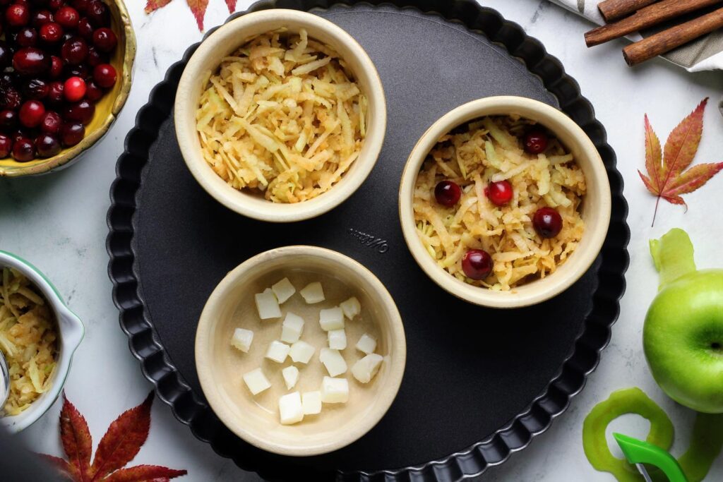 Layering butter, shredded apples, and cranberries in eight-ounce ramekins