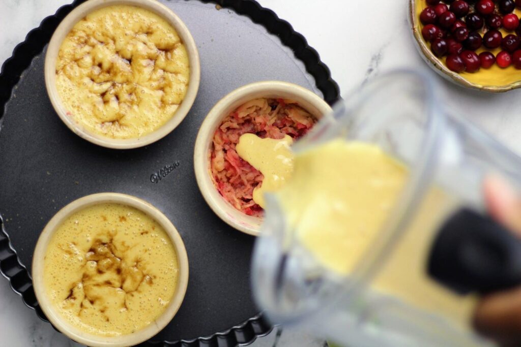 Pouring the puffed pancake batter over the mixture of shredded apples, smashed cranberries, and butter.