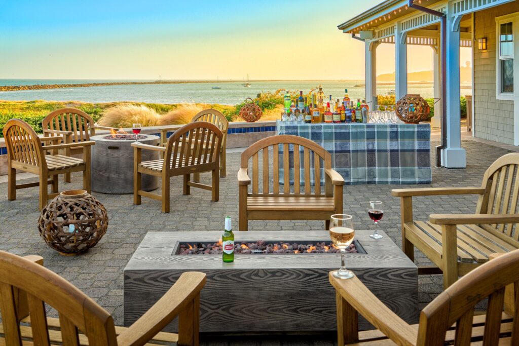 Patio with fire pit, seating and views of sunset over the ocean.