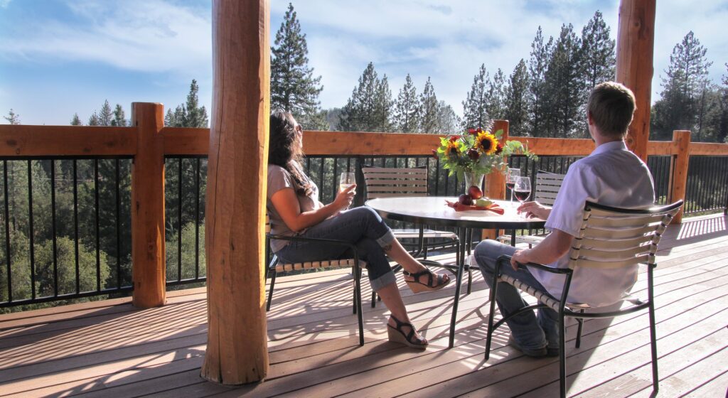 A couple seated at a table with wine on a deck overlooking a forest