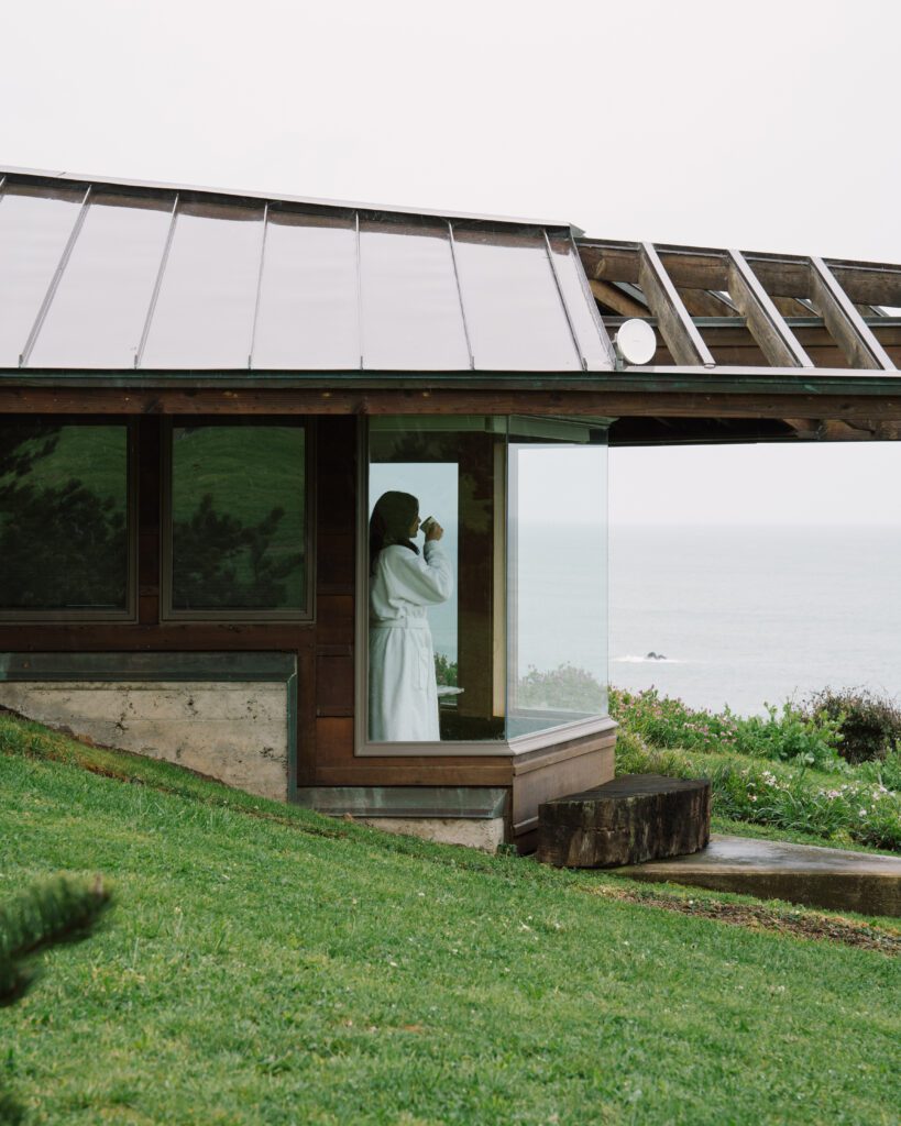 Woman in a bathrobe looking out at the ocean from her room with a cup of coffee