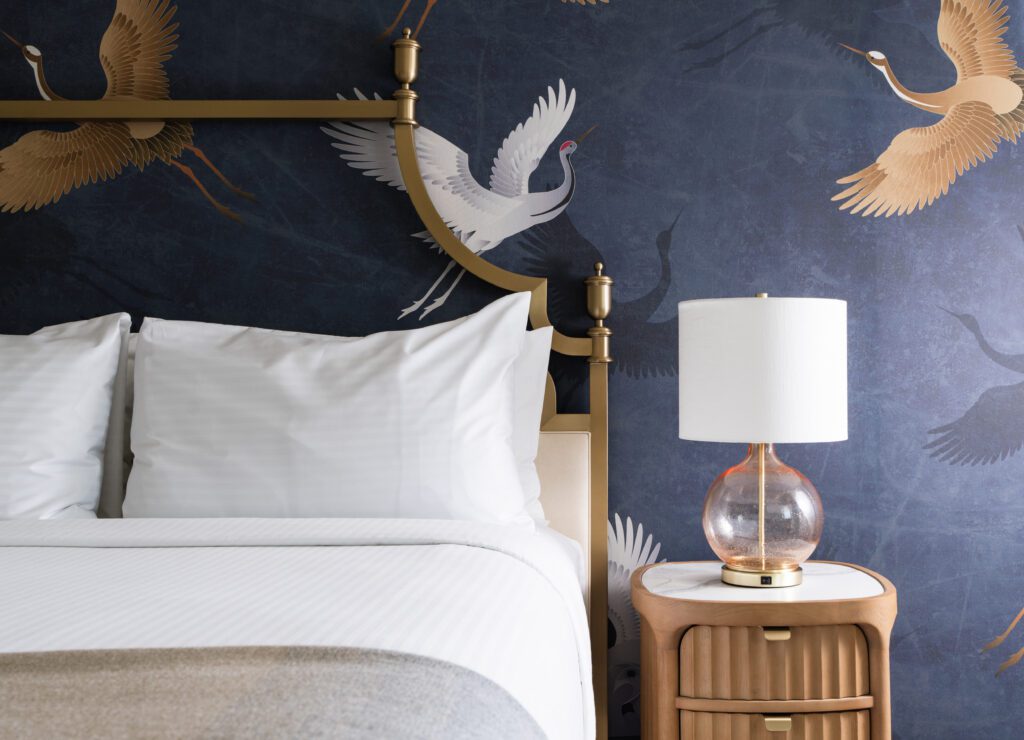 Guest room detail at The Milo with wallcoverings of herons in flight and a pale pink glass lamp
